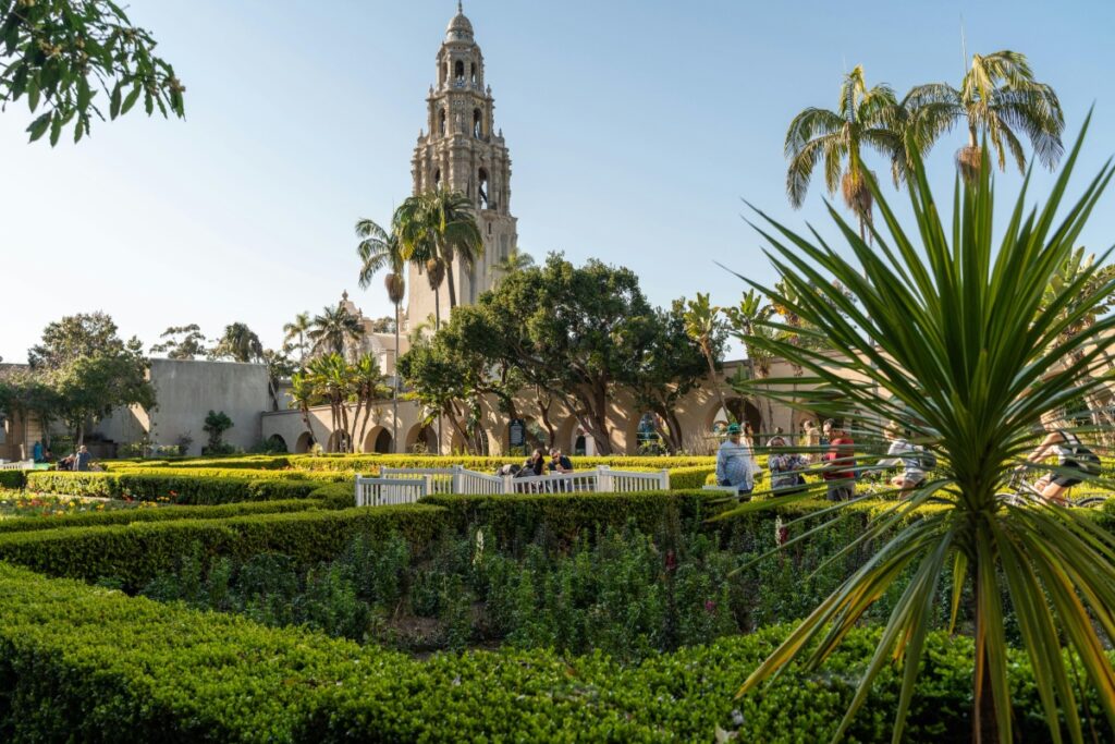 Esta imagen muestra un bonito jardín con setos bien recortados y palmeras, con un impresionante edificio con una torre en el fondo. Es un lugar tranquilo y atractivo, probablemente un centro cultural o histórico. Para profesionales en Chile que buscan generar oportunidades B2B a través de LinkedIn, compartiendo contenido relacionado con estos lugares turísticos y culturales, siguiendo las estrategias de "LinkedIn en Chile Cómo Generar Oportunidades B2B", puede ser una forma efectiva de conectarse con otros negocios y crear relaciones mutually beneficiosas.