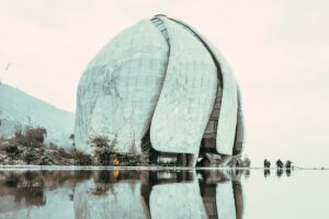 Esta imagen presenta un moderno edificio de forma esférica y sinuosa, con una textura de placas que lo hace muy atractivo visualmente. Está rodeado de una superficie de agua que refleja el edificio, y se ven algunas personas cerca. Para las marcas en Chile en 2025, Snapchat puede ser una herramienta útil. Compartiendo contenido de lugares modernos e interesantes como este a través de Snapchat, siguiendo las estrategias que responden a la pregunta &ldquo;Snapchat en Chile ¿Es útil para tu marca en 2025&rdquo;, se puede alcanzar a un público joven y activo, aumentando la visibilidad y la interacción con la marca.